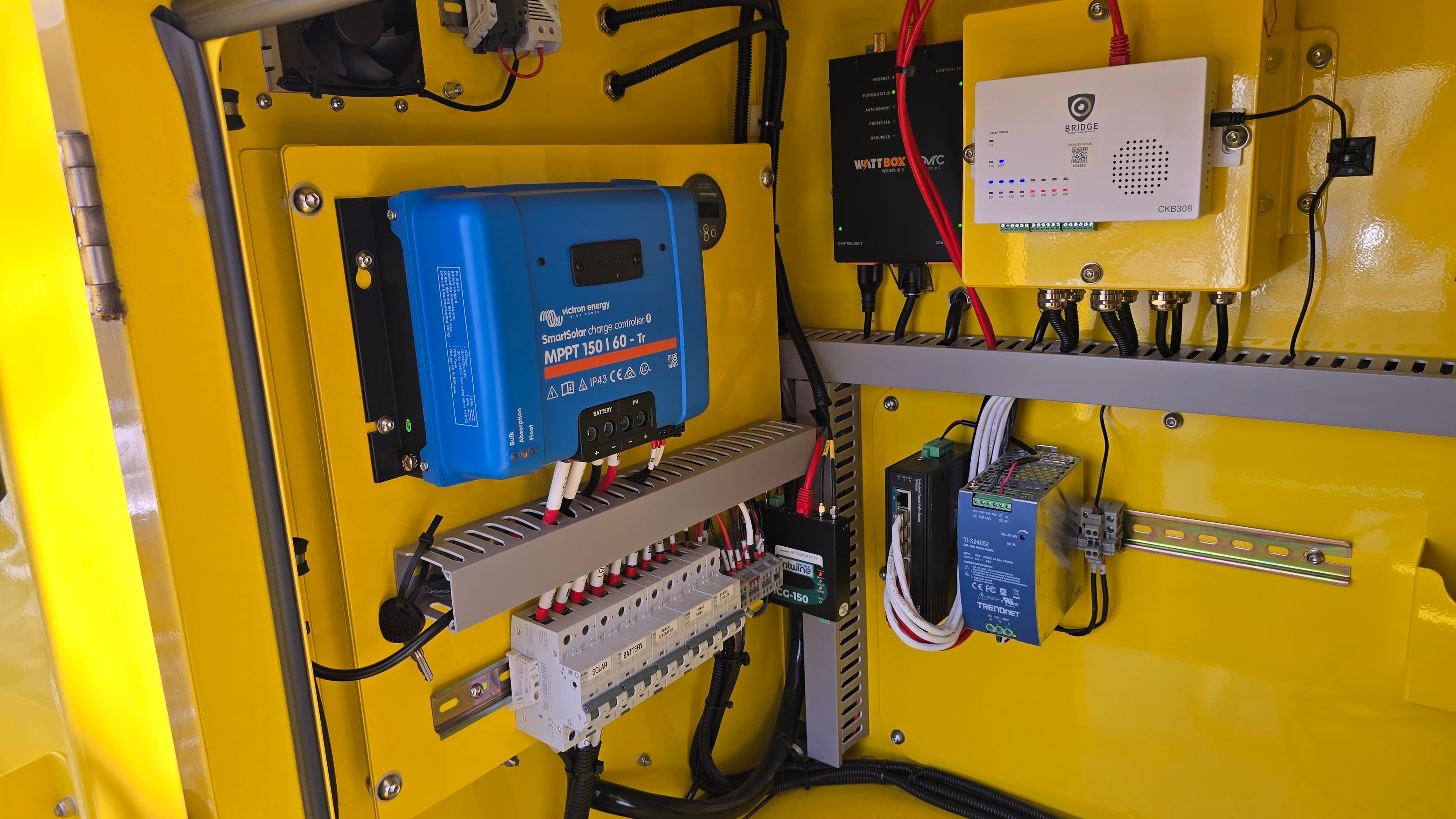 Yellow electrical enclosure housing a blue solar charge controller, circuit breakers, and various networking components.