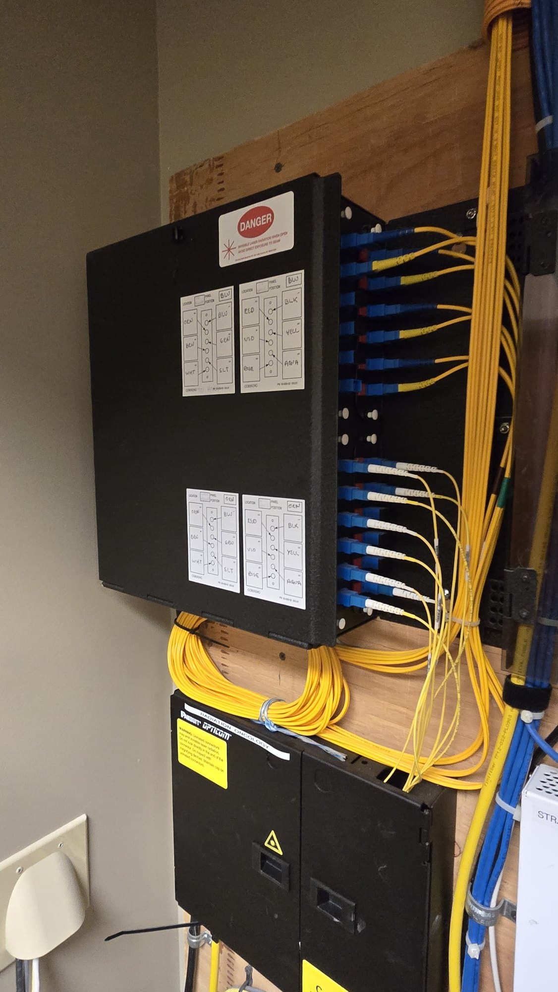 Black fiber optic patch panel with neatly organized yellow cables and handwritten identification labels.