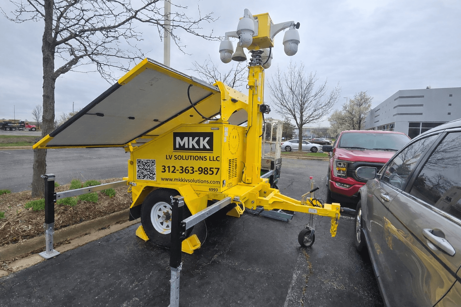 Bright yellow mobile security trailer with solar panels and surveillance cameras in a parking lot.